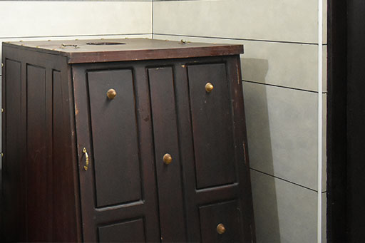 A dark wooden medicine cabinet with brass handles, in the corner of a treatment room