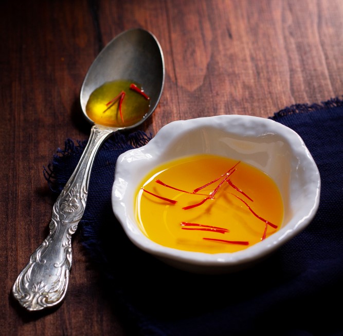 Saffron strands steeped in golden ghrita, with a silver spoon alongside
